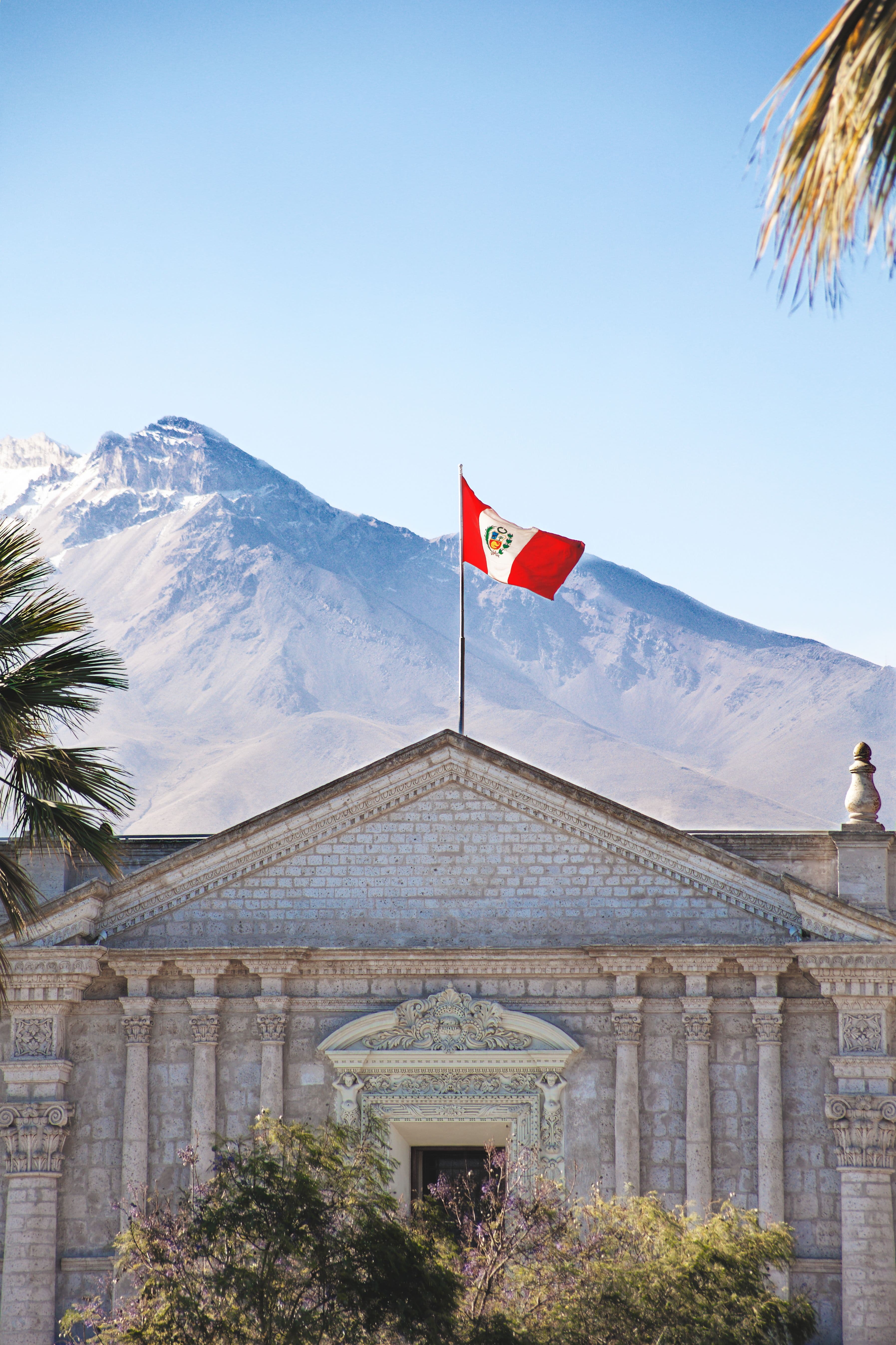 Peruvian flag above stone architecture with mountains in the background